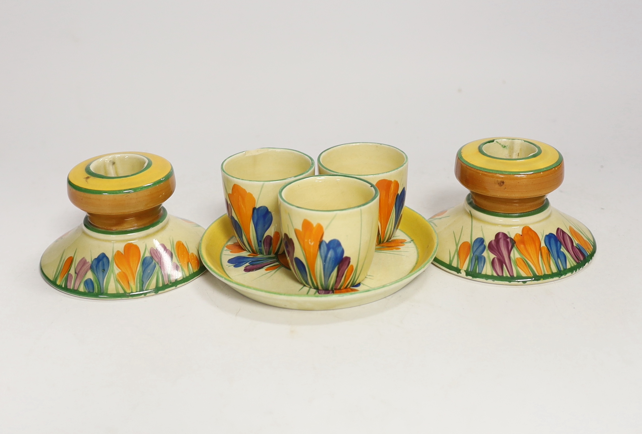 Clarice Cliff Crocus pattern items; a pair of candlesticks, 5cm high and three egg cups with stand